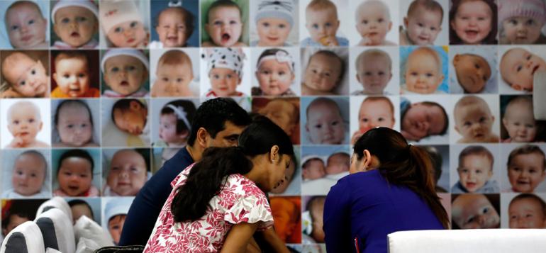 Tre voksne i samtale foran vegg dekket av babyportretter